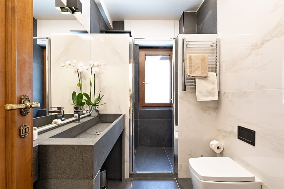 Cette image montre une grande salle de bain principale design avec un placard sans porte, des portes de placard grises, une douche double, WC suspendus, un carrelage noir et blanc, des carreaux de porcelaine, un mur blanc, un sol en carrelage de porcelaine, une grande vasque, un plan de toilette en marbre, un sol gris, une cabine de douche à porte battante, un plan de toilette gris, un banc de douche, meuble simple vasque et meuble-lavabo sur pied.