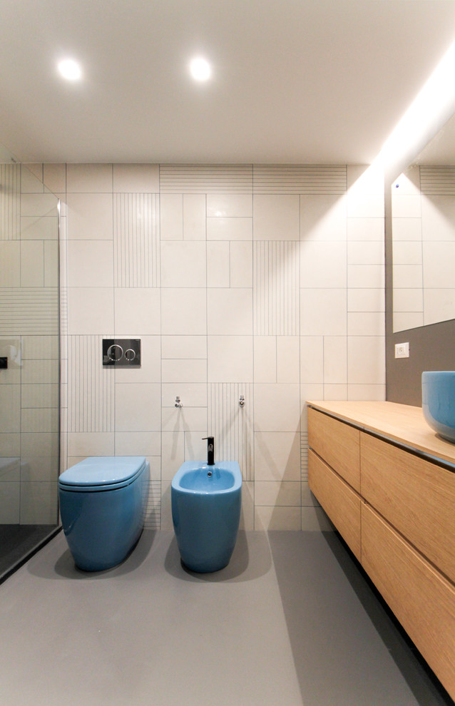 Cette image montre une salle d'eau design en bois clair avec un placard à porte affleurante, une douche ouverte, WC à poser, un carrelage multicolore, des carreaux de porcelaine, un mur multicolore, sol en béton ciré, une vasque, un plan de toilette en bois, un sol gris et aucune cabine.