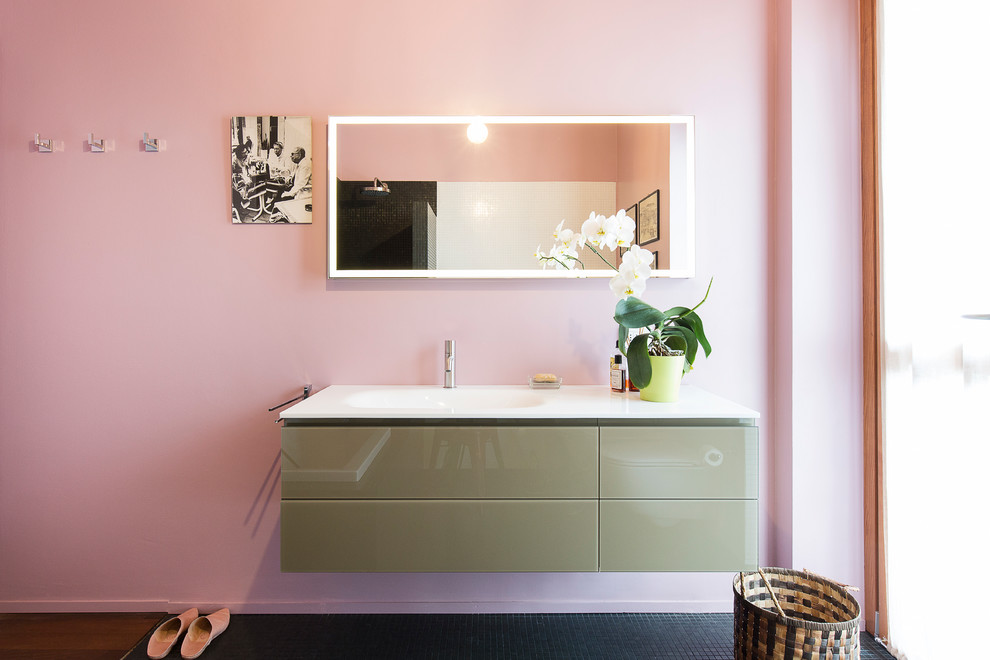 Cette photo montre une salle de bain principale tendance de taille moyenne avec une baignoire posée, WC suspendus, un carrelage noir, mosaïque, un mur rose, un lavabo intégré, un plan de toilette en verre, un sol vert et un plan de toilette blanc.