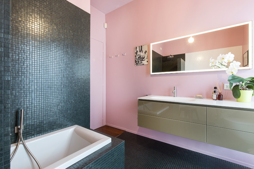 Ispirazione per una stanza da bagno padronale minimal di medie dimensioni con vasca da incasso, WC sospeso, piastrelle nere, piastrelle a mosaico, pareti rosa, lavabo integrato, top in vetro, pavimento verde e top bianco