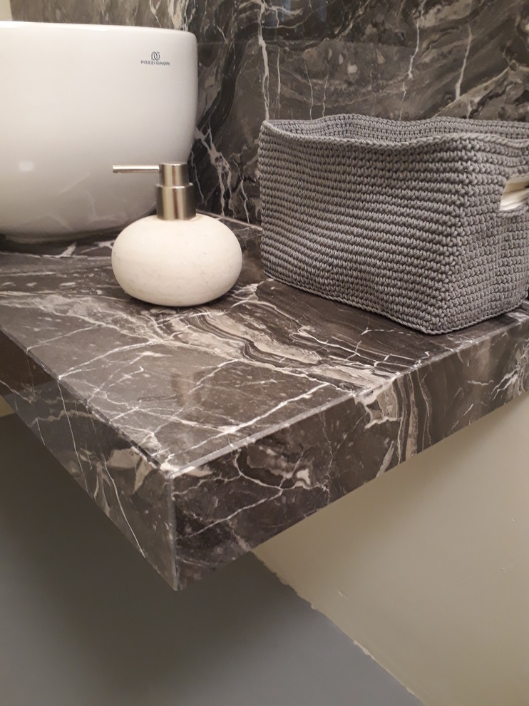 Bild på ett litet industriellt grå grått badrum, med öppna hyllor, en dusch i en alkov, en toalettstol med separat cisternkåpa, grå kakel, marmorkakel, beige väggar, ett fristående handfat, marmorbänkskiva, grått golv och dusch med gångjärnsdörr