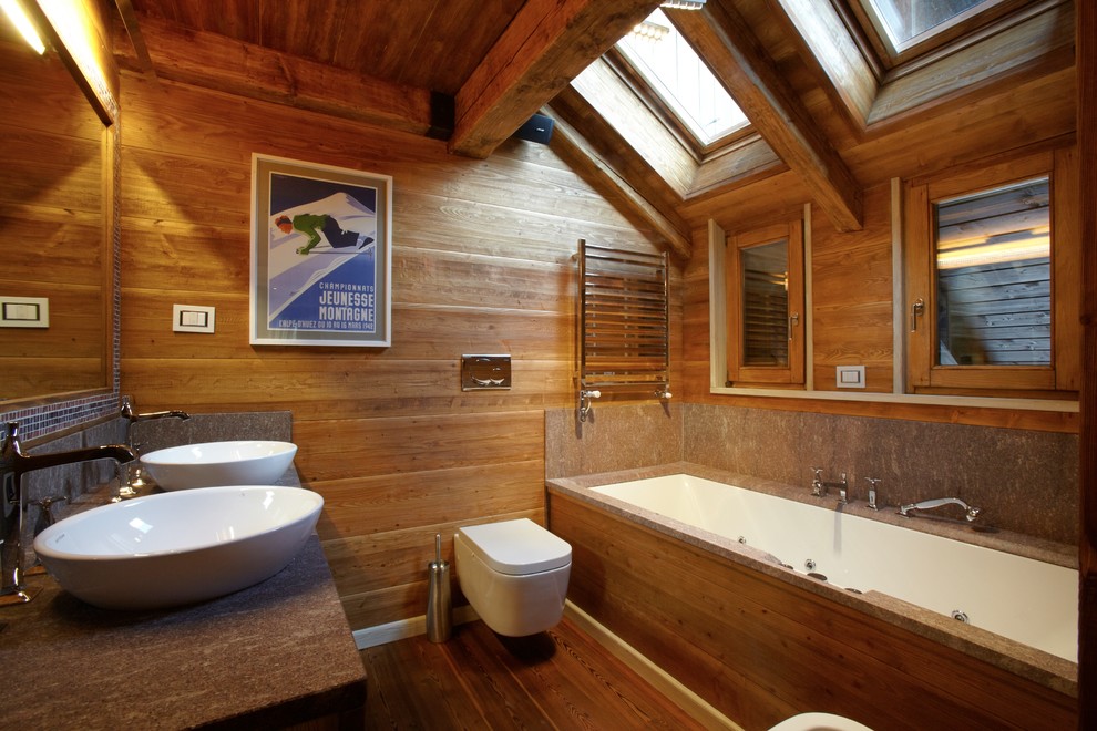 Rustik inredning av ett badrum, med ett undermonterat badkar, en vägghängd toalettstol, mellanmörkt trägolv och ett fristående handfat