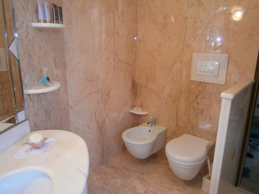 Klassisk inredning av ett stort rosa rosa badrum med dusch, med luckor med infälld panel, skåp i ljust trä, en kantlös dusch, en toalettstol med separat cisternkåpa, rosa kakel, marmorkakel, rosa väggar, marmorgolv, ett undermonterad handfat, marmorbänkskiva, rosa golv och dusch med gångjärnsdörr