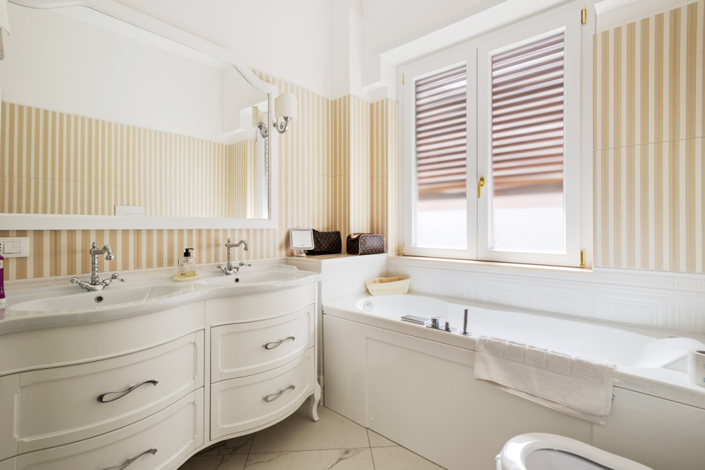 Aménagement d'une salle de bain principale classique de taille moyenne avec un placard en trompe-l'oeil, des portes de placard blanches, un bain bouillonnant, une douche d'angle, un bidet, un carrelage gris, des carreaux en allumettes, un mur jaune, un sol en carrelage de porcelaine, un plan vasque, un sol multicolore, une cabine de douche à porte battante, un plan de toilette blanc, meuble double vasque, meuble-lavabo sur pied et boiseries.