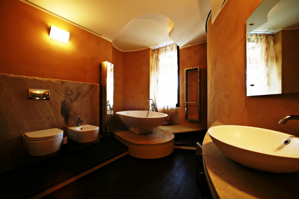 На фото: большая главная ванная комната в стиле модернизм с отдельно стоящей ванной, открытым душем, инсталляцией, плиткой из листового камня, оранжевыми стенами, темным паркетным полом, настольной раковиной и столешницей из талькохлорита