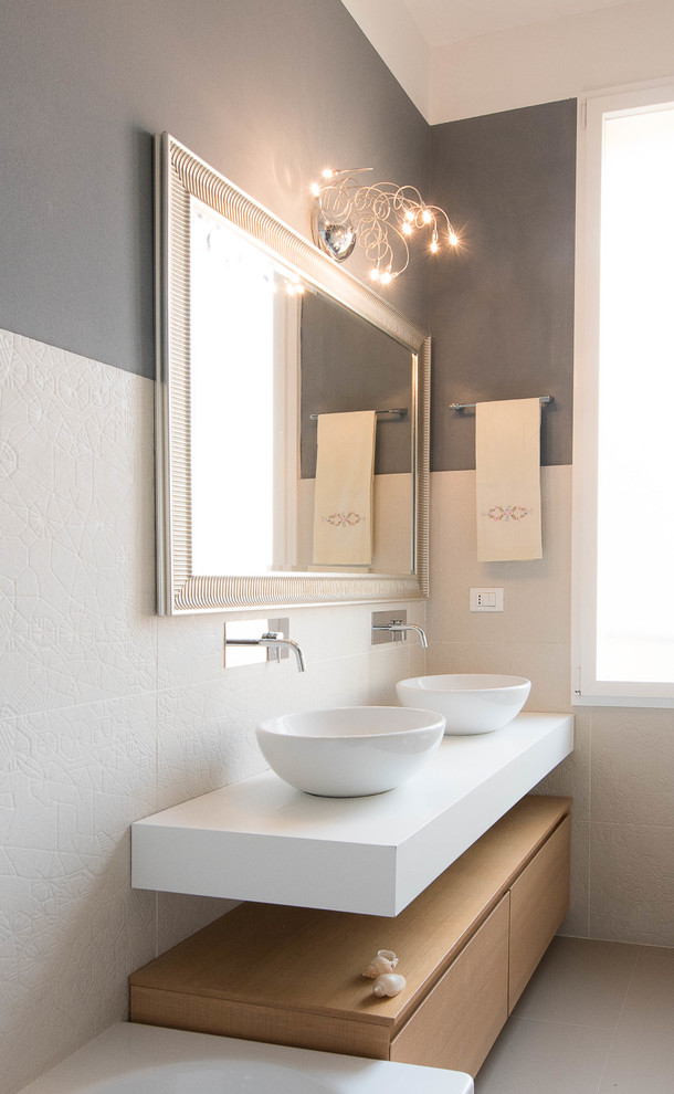 Modern inredning av ett vit vitt badrum, med skåp i ljust trä, klinkergolv i porslin, ett fristående handfat, släta luckor, vit kakel, grå väggar och grått golv
