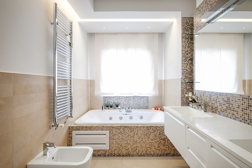 Esempio di una stanza da bagno padronale design di medie dimensioni con ante bianche, vasca/doccia, piastrelle multicolore, piastrelle a mosaico, pareti bianche, lavabo integrato, pavimento beige, doccia aperta, ante lisce, vasca idromassaggio, WC sospeso, pavimento in gres porcellanato, top in superficie solida e top bianco