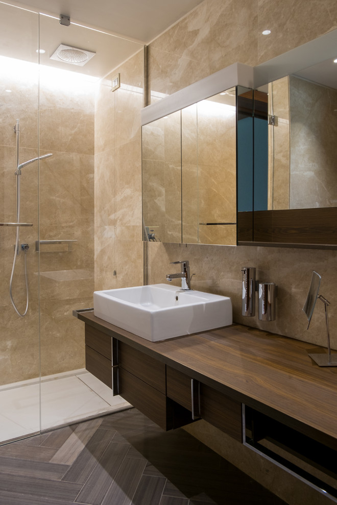 Exempel på ett mellanstort modernt brun brunt badrum med dusch, med släta luckor, skåp i mörkt trä, beige kakel, stenhäll, träbänkskiva, en dusch i en alkov, ett fristående handfat, en vägghängd toalettstol och marmorgolv