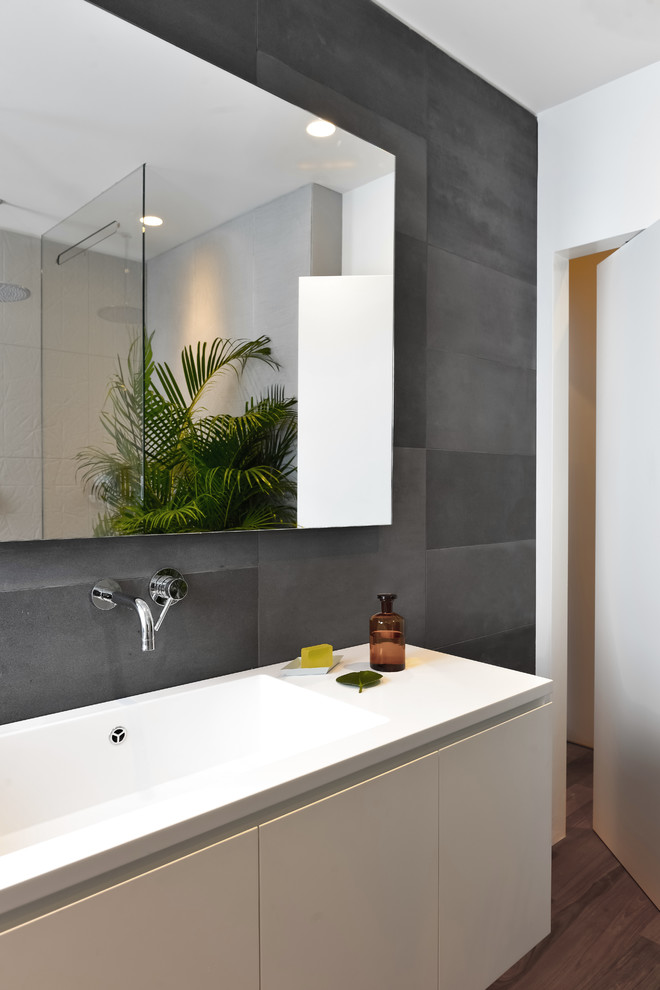 Diseño de cuarto de baño actual con armarios con paneles lisos, puertas de armario blancas, baldosas y/o azulejos grises, paredes blancas, suelo de madera oscura y lavabo integrado