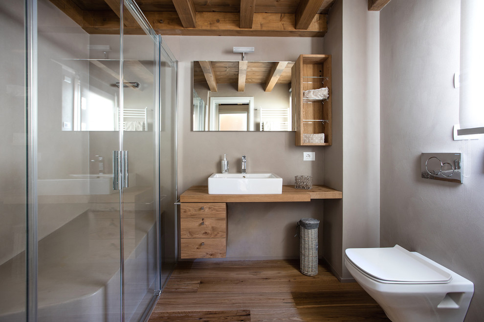 Idée de décoration pour une grande salle de bain grise et blanche chalet en bois brun avec un placard à porte plane, une douche d'angle, WC suspendus, un mur gris, un sol en bois brun et une vasque.