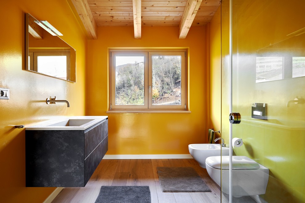 Ejemplo de cuarto de baño principal contemporáneo grande con armarios con paneles lisos, puertas de armario grises, sanitario de pared, paredes amarillas, suelo de madera en tonos medios y lavabo encastrado