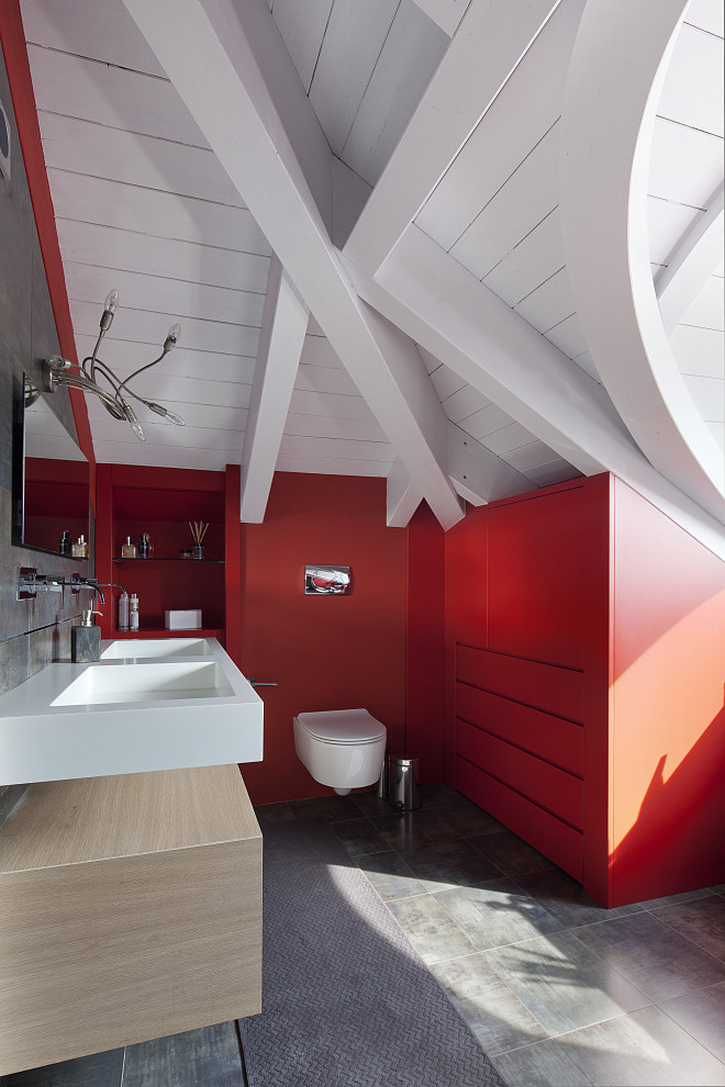 Inredning av ett modernt mellanstort vit vitt en-suite badrum, med en vägghängd toalettstol, röda väggar, klinkergolv i keramik, bänkskiva i akrylsten, grått golv, skåp i ljust trä och ett integrerad handfat