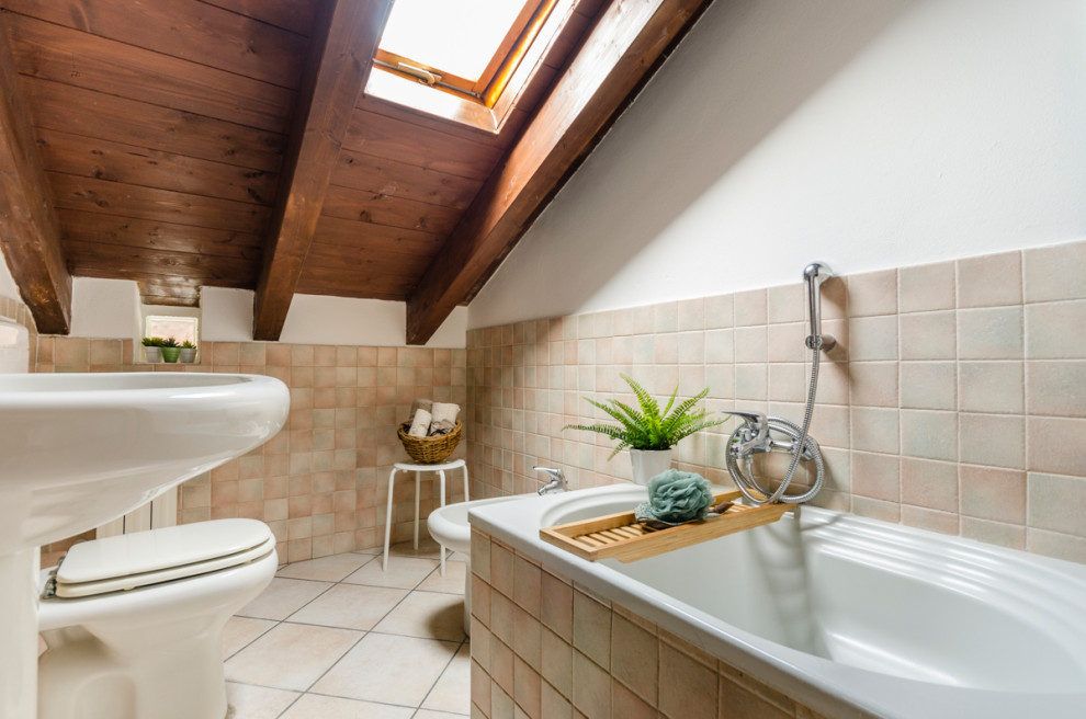 Immagine di una stanza da bagno mediterranea di medie dimensioni con vasca da incasso, bidè, piastrelle beige, pareti bianche, lavabo a colonna e pavimento beige