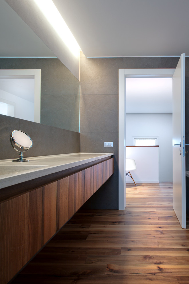 Réalisation d'une salle de bain design en bois brun de taille moyenne avec un placard à porte plane, un mur gris, un sol en bois brun, un lavabo intégré et un plan de toilette en marbre.