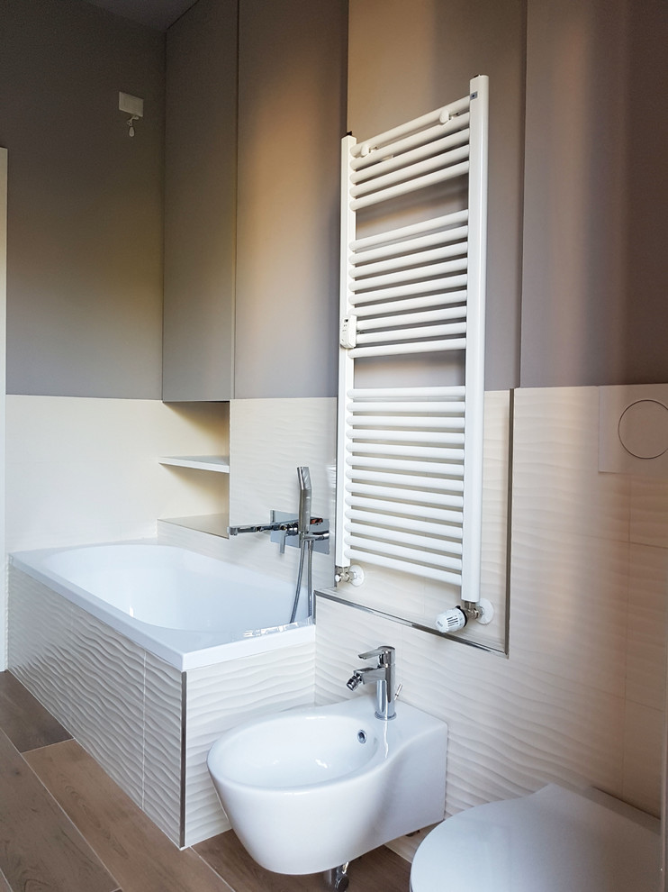 This is an example of a large contemporary ensuite bathroom in Milan with flat-panel cabinets, white cabinets, a built-in bath, a wall mounted toilet, white tiles, porcelain tiles, grey walls, porcelain flooring, a vessel sink, laminate worktops, brown floors and white worktops.