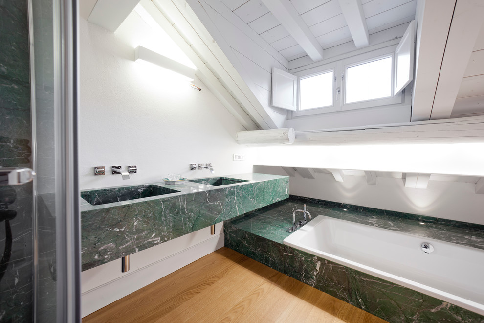 Example of a trendy master stone slab medium tone wood floor drop-in bathtub design in Milan with white walls and marble countertops