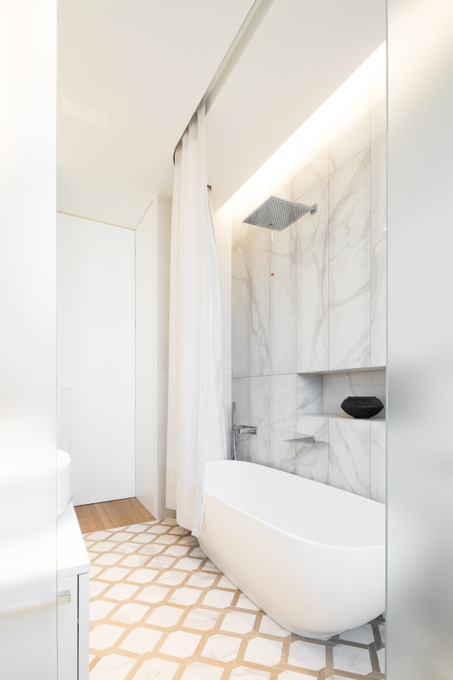 Inredning av ett modernt mycket stort vit vitt en-suite badrum, med släta luckor, vita skåp, ett badkar i en alkov, en dusch i en alkov, en toalettstol med separat cisternkåpa, vit kakel, marmorkakel, vita väggar, marmorgolv, ett fristående handfat, marmorbänkskiva, vitt golv och dusch med duschdraperi
