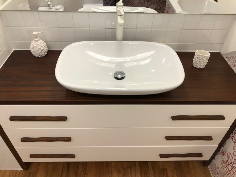 Bild på ett litet maritimt brun brunt badrum, med släta luckor, vita skåp, ett badkar i en alkov, en toalettstol med separat cisternkåpa, röd kakel, vita väggar, mörkt trägolv, ett fristående handfat, träbänkskiva och brunt golv