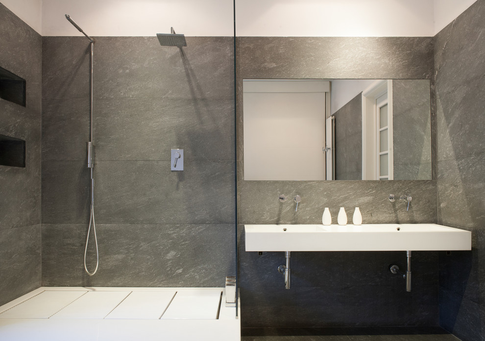 Modern inredning av ett badrum, med en hörndusch, grå kakel, stenhäll och ett väggmonterat handfat