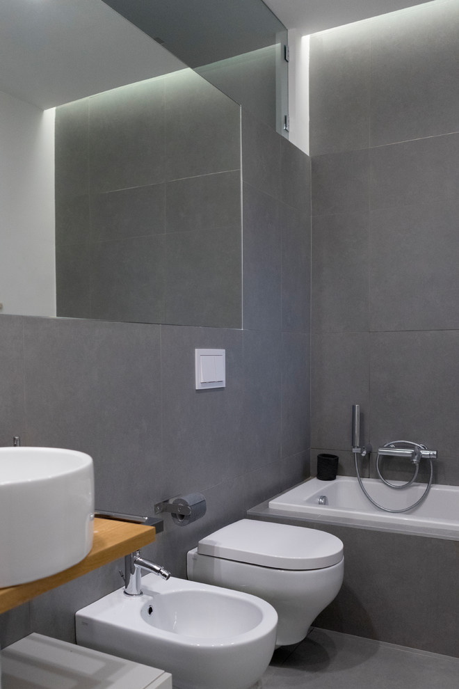 Idéer för mellanstora funkis en-suite badrum, med släta luckor, vita skåp, ett platsbyggt badkar, en dusch/badkar-kombination, en vägghängd toalettstol, grå kakel, porslinskakel, grå väggar, klinkergolv i porslin, ett fristående handfat, träbänkskiva, grått golv och med dusch som är öppen