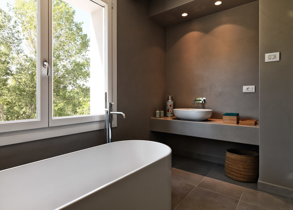 Modelo de cuarto de baño principal y de obra actual con bañera exenta, paredes grises, lavabo sobreencimera, suelo gris y encimeras grises