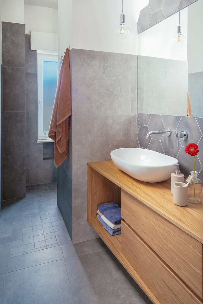 Urban 3/4 gray tile porcelain tile and gray floor bathroom photo in Naples with flat-panel cabinets, light wood cabinets, a wall-mount toilet, gray walls, a vessel sink and wood countertops