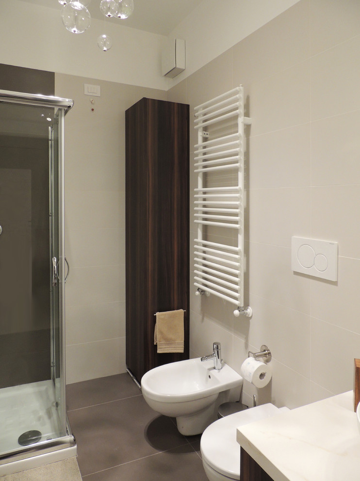 Small traditional shower room bathroom in Bari with beaded cabinets, brown cabinets, a corner shower, a wall mounted toilet, beige tiles, ceramic tiles, white walls, ceramic flooring, a vessel sink, tiled worktops, brown floors and a sliding door.