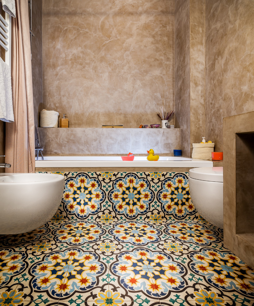 Ispirazione per una stanza da bagno per bambini mediterranea di medie dimensioni con vasca ad alcova, vasca/doccia, bidè, pareti beige, pavimento con piastrelle in ceramica, pavimento multicolore e doccia con tenda