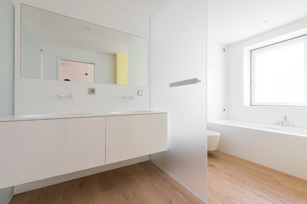 Стильный дизайн: большая главная ванная комната в современном стиле с плоскими фасадами, белыми фасадами, ванной в нише, душем без бортиков, инсталляцией, белой плиткой, стеклянной плиткой, желтыми стенами, светлым паркетным полом, монолитной раковиной, коричневым полом и открытым душем - последний тренд