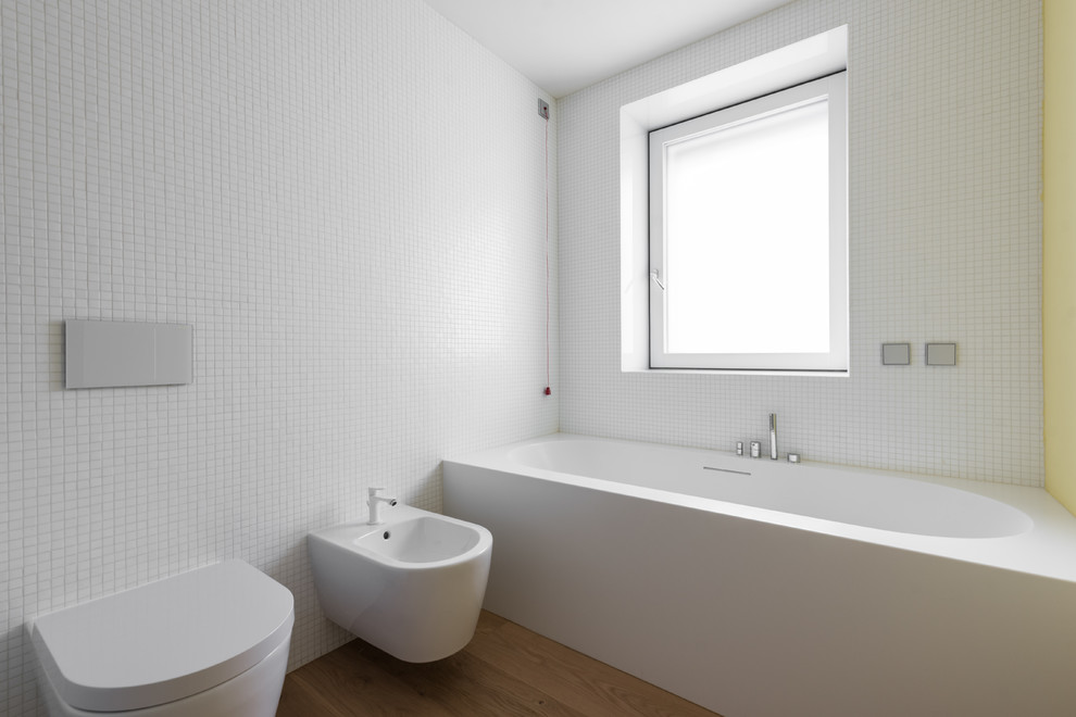 This is an example of a large contemporary ensuite bathroom in Other with flat-panel cabinets, white cabinets, an alcove bath, a built-in shower, a wall mounted toilet, white tiles, glass tiles, yellow walls, light hardwood flooring, an integrated sink, brown floors and an open shower.