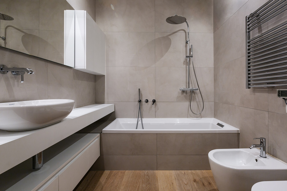 Idéer för mellanstora funkis vitt en-suite badrum, med släta luckor, vita skåp, porslinskakel, ett fristående handfat, ett badkar i en alkov, en dusch/badkar-kombination, en bidé, grå kakel, grå väggar, mellanmörkt trägolv, brunt golv och med dusch som är öppen