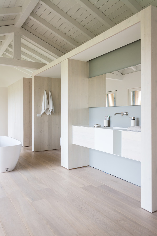 Foto på ett stort funkis en-suite badrum, med släta luckor, skåp i ljust trä, ett fristående badkar, grå väggar, ljust trägolv och ett väggmonterat handfat