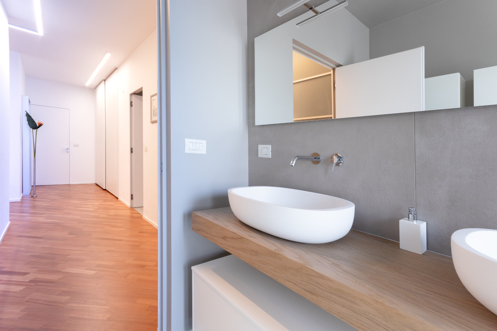Doorless shower - large contemporary master gray tile and porcelain tile porcelain tile and gray floor doorless shower idea in Milan with flat-panel cabinets, white cabinets, a two-piece toilet, gray walls, a vessel sink, wood countertops, a hinged shower door and white countertops