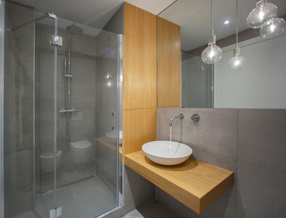 Inspiration för små moderna brunt badrum med dusch, med släta luckor, skåp i ljust trä, grå kakel, grå väggar, ett fristående handfat, träbänkskiva, grått golv, en dusch i en alkov och dusch med gångjärnsdörr