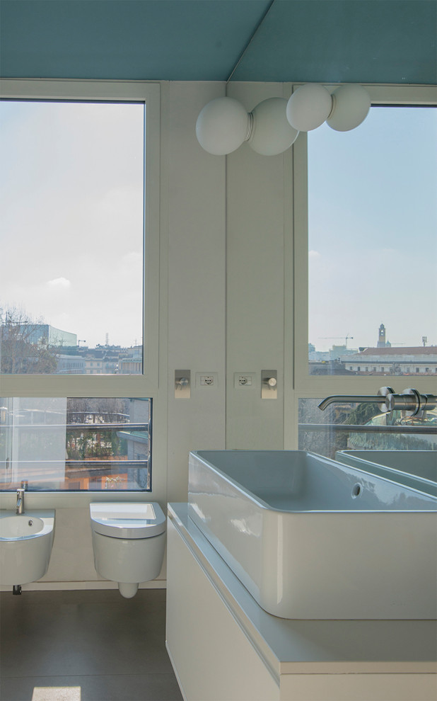 Cette image montre une salle de bain design avec un placard à porte plane, des portes de placard blanches, un bidet, un mur blanc, une vasque, un sol gris, un plan de toilette blanc, meuble simple vasque et meuble-lavabo suspendu.