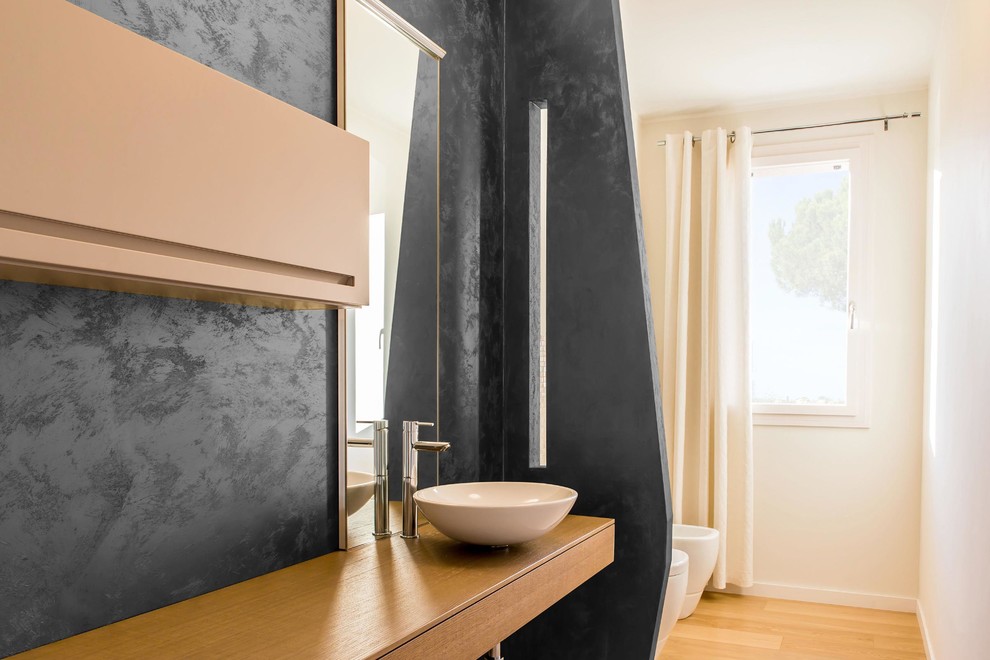 Immagine di una stanza da bagno minimal con ante in legno chiaro, WC a due pezzi, pareti nere, parquet chiaro, lavabo a bacinella e top in legno