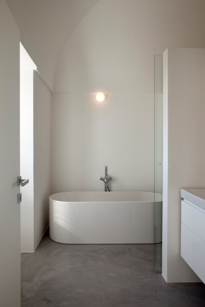 На фото: главная ванная комната среднего размера в стиле модернизм с фасадами с декоративным кантом, белыми фасадами, отдельно стоящей ванной, душем без бортиков, инсталляцией, белой плиткой, мраморной плиткой, белыми стенами, бетонным полом, монолитной раковиной, серым полом, душем с распашными дверями, белой столешницей, тумбой под две раковины, напольной тумбой и сводчатым потолком