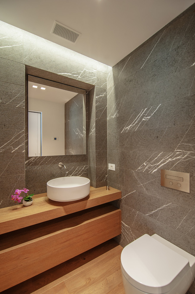 Bathroom - contemporary gray tile bathroom idea in Venice with wood countertops, a wall-mount toilet, a vessel sink, medium tone wood cabinets and brown countertops