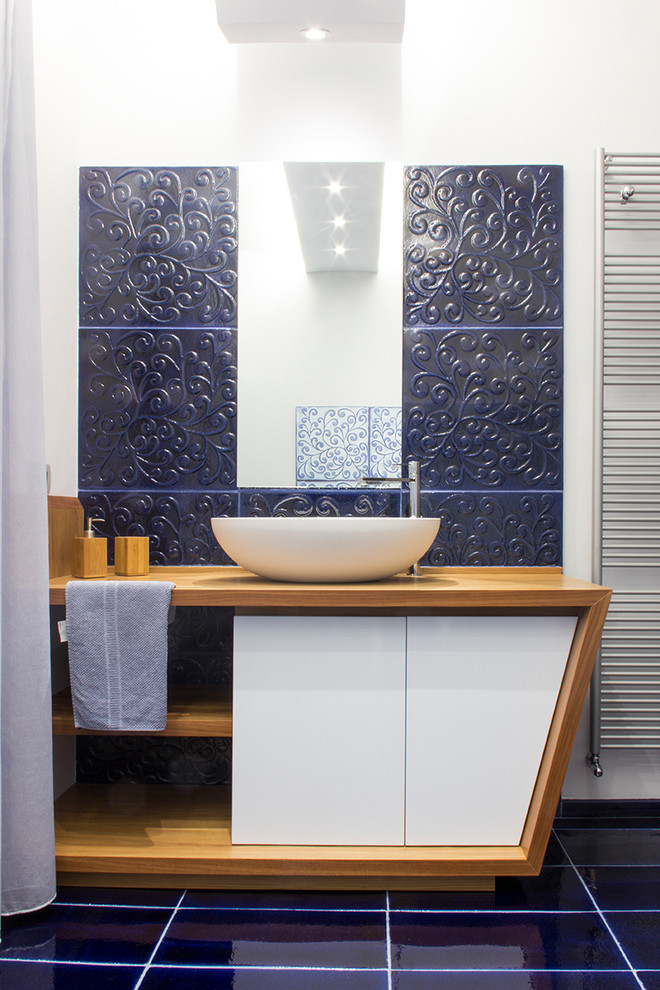 Imagen de cuarto de baño actual con puertas de armario de madera oscura, baldosas y/o azulejos azules, paredes blancas, lavabo sobreencimera, suelo azul, armarios con paneles lisos, aseo y ducha y encimera de madera