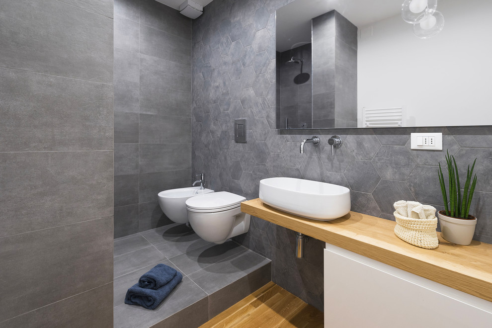 Inspiration for a modern shower room bathroom in Florence with flat-panel cabinets, white cabinets, an alcove shower, a wall mounted toilet, grey walls, light hardwood flooring, a vessel sink, wooden worktops, beige floors, an open shower and beige worktops.