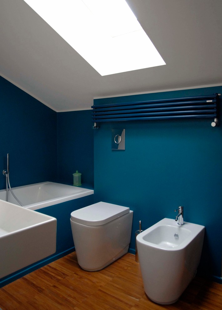 Foto di una piccola stanza da bagno contemporanea con vasca da incasso, WC a due pezzi, pareti blu, pavimento in legno massello medio, lavabo rettangolare e pavimento marrone
