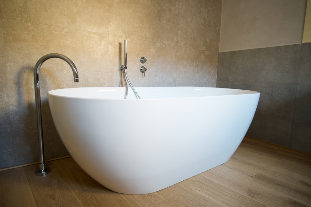 Aménagement d'une grande salle de bain principale contemporaine avec une baignoire indépendante, un carrelage beige, des carreaux de céramique, un mur gris, parquet clair et un sol marron.