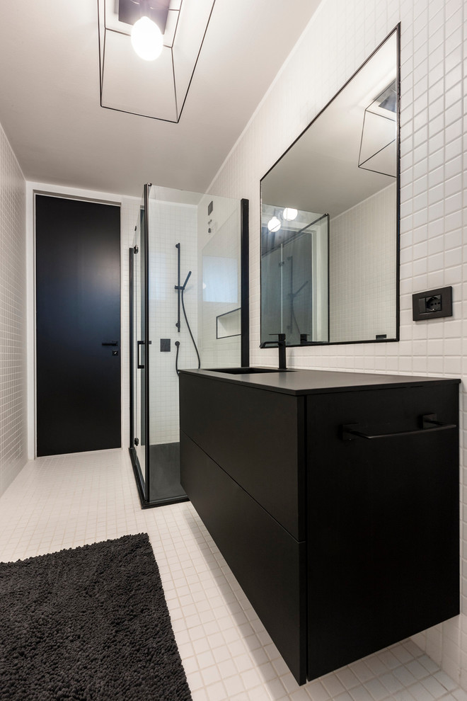 На фото: ванная комната в стиле модернизм с плоскими фасадами, черными фасадами, угловым душем, белой плиткой, белыми стенами, душевой кабиной, монолитной раковиной, белым полом, душем с распашными дверями и черной столешницей с