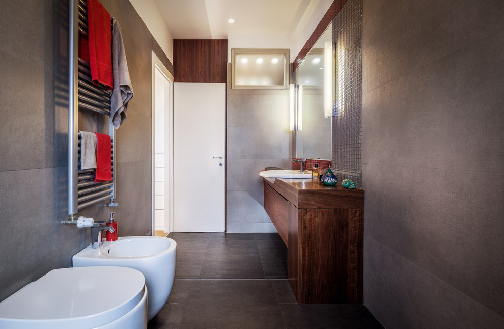 Inspiration pour une salle d'eau design en bois foncé de taille moyenne avec un placard à porte plane, un bidet, un carrelage gris, un mur blanc, un lavabo posé, un plan de toilette en bois, un sol gris et un plan de toilette marron.