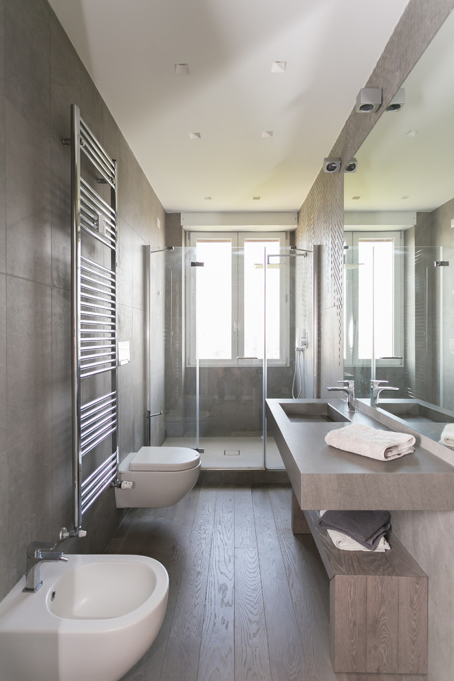 Exemple d'une salle de bain tendance de taille moyenne avec un placard sans porte, un carrelage gris, un mur gris, un lavabo intégré, une cabine de douche à porte battante, des portes de placard grises, WC suspendus, parquet foncé et un sol marron.