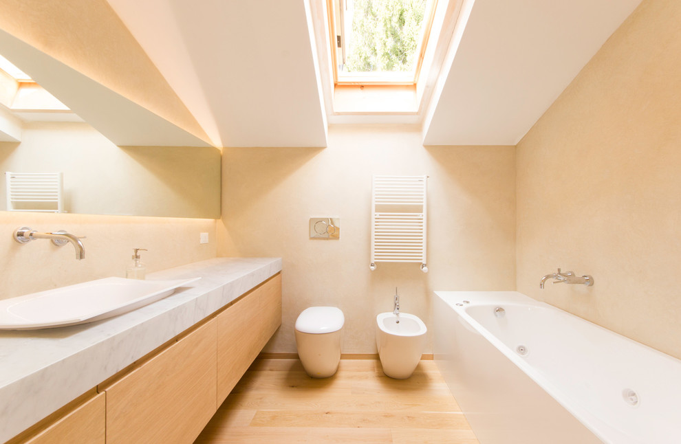 Foto på ett skandinaviskt badrum, med släta luckor, skåp i ljust trä, en bidé, beige väggar, ljust trägolv och ett fristående handfat