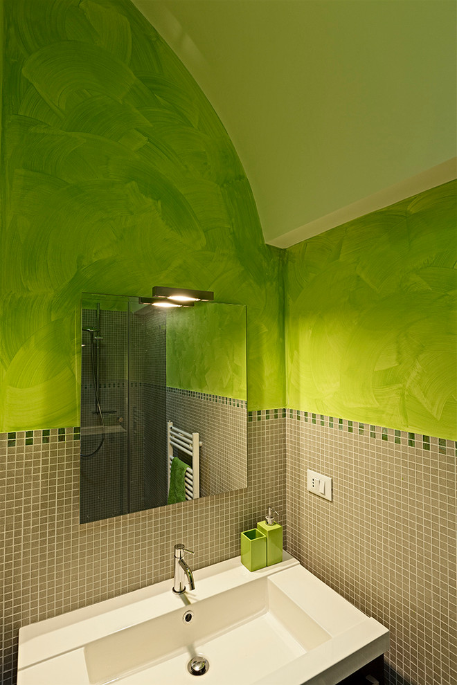 Photo of a small mediterranean shower room bathroom in Bari with flat-panel cabinets, an alcove shower, a two-piece toilet, beige tiles, porcelain tiles, green walls, medium hardwood flooring, an integrated sink and solid surface worktops.