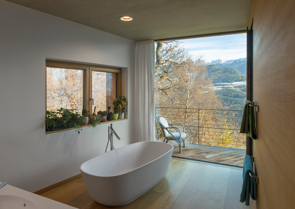 Modernes Badezimmer mit freistehender Badewanne, weißer Wandfarbe und braunem Holzboden in Sonstige