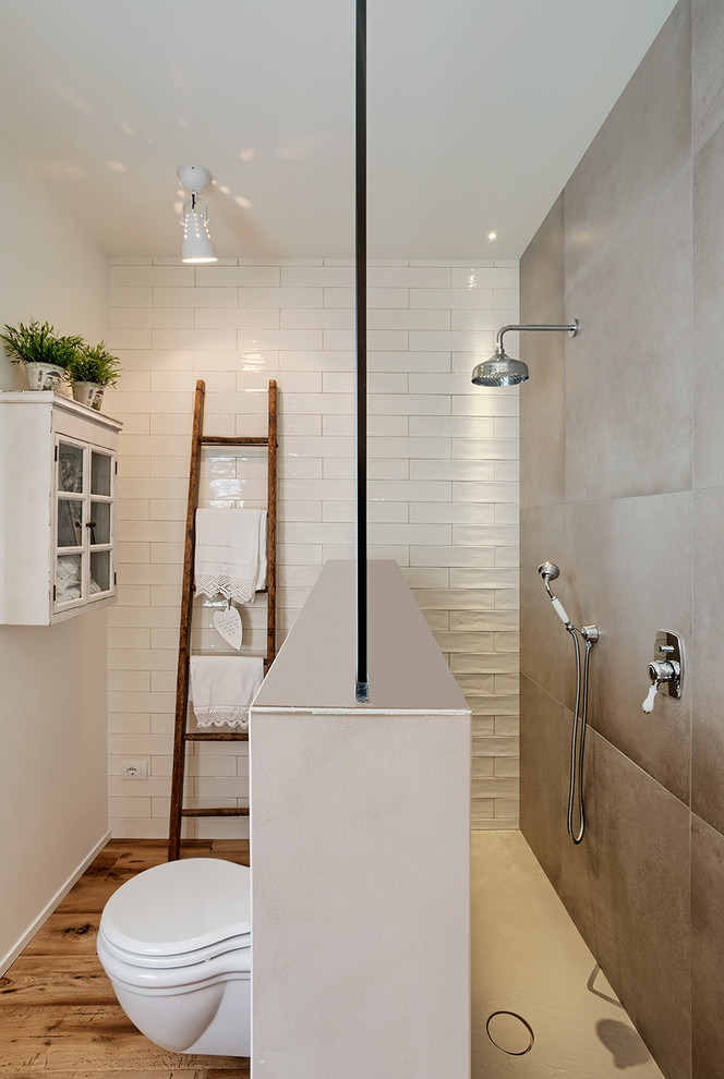 Cette image montre une salle d'eau style shabby chic de taille moyenne avec une douche ouverte, WC suspendus, un carrelage beige, un carrelage blanc, des carreaux de céramique, un mur blanc, un sol en bois brun et un sol marron.