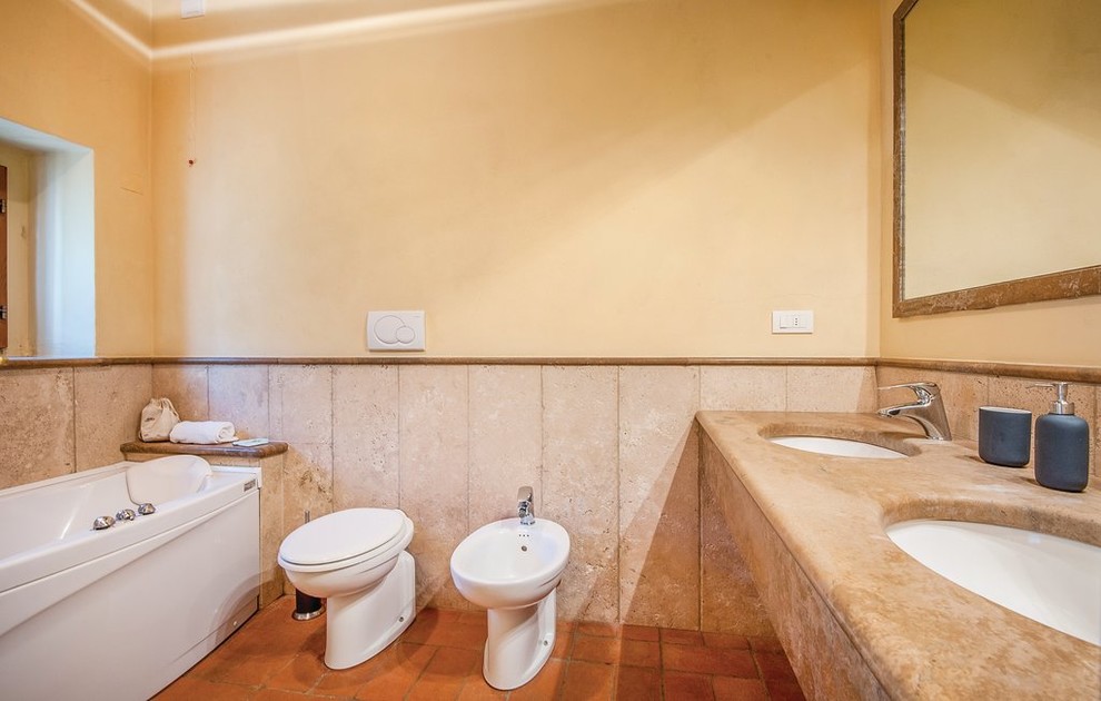 Lantlig inredning av ett mellanstort beige beige en-suite badrum, med en jacuzzi, en dusch/badkar-kombination, en toalettstol med separat cisternkåpa, beige kakel, marmorkakel, klinkergolv i terrakotta, ett fristående handfat, marmorbänkskiva, rött golv och dusch med skjutdörr